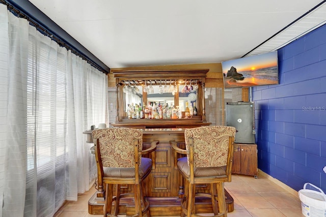 bar with a dry bar, light tile patterned floors, and concrete block wall