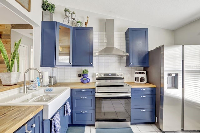 kitchen featuring glass insert cabinets, appliances with stainless steel finishes, blue cabinets, wall chimney range hood, and a sink