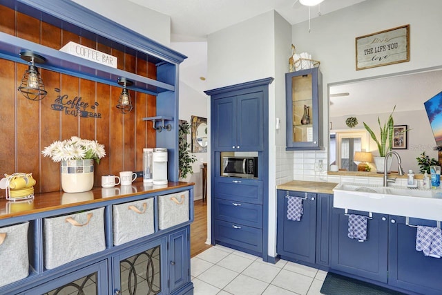 kitchen with glass insert cabinets, blue cabinets, stainless steel microwave, and a sink