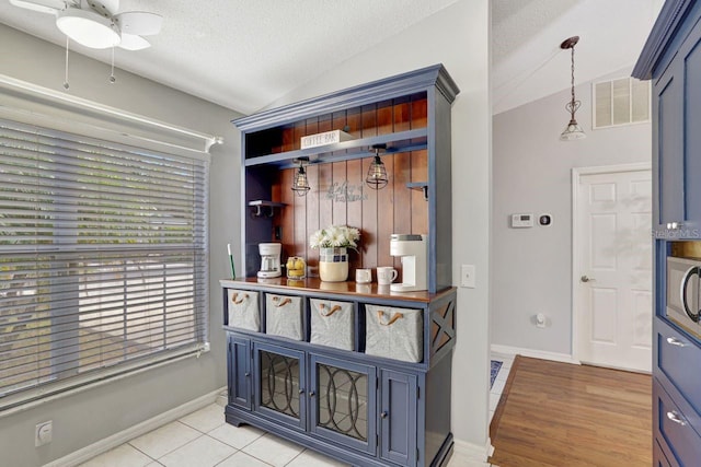 interior space featuring a textured ceiling, visible vents, vaulted ceiling, blue cabinetry, and decorative light fixtures