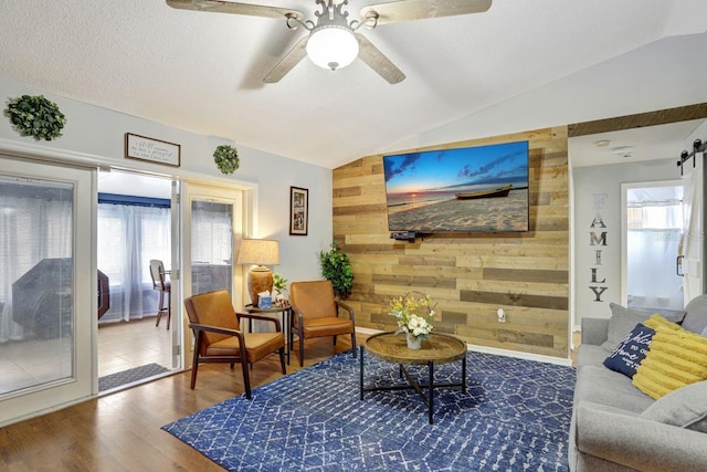 living area with lofted ceiling, plenty of natural light, wooden walls, and a textured ceiling