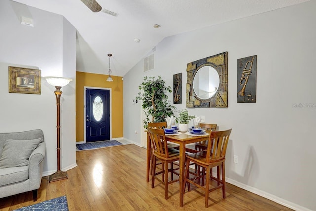 dining space featuring baseboards, visible vents, vaulted ceiling, and wood finished floors