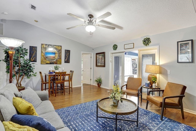 living area with ceiling fan, a textured ceiling, dark wood-style flooring, visible vents, and vaulted ceiling