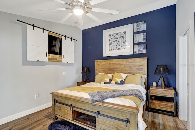 bedroom with wood finished floors, ceiling fan, baseboards, and a barn door