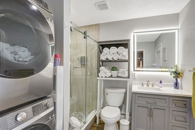 bathroom featuring toilet, a stall shower, vanity, and stacked washer and clothes dryer