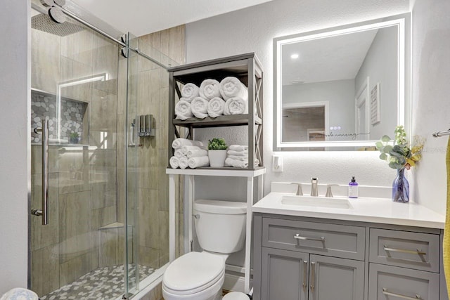 bathroom featuring toilet, a stall shower, a textured wall, and vanity