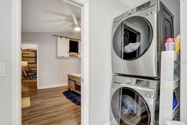 washroom featuring stacked washer and dryer, ceiling fan, wood finished floors, laundry area, and baseboards