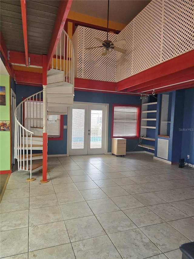 unfurnished living room with a ceiling fan, a towering ceiling, stairway, tile patterned flooring, and french doors