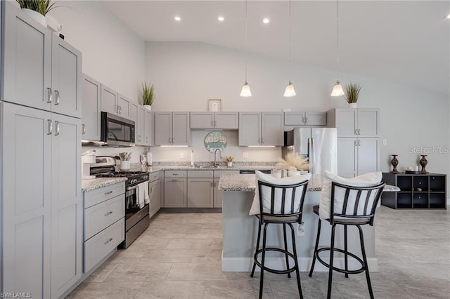 kitchen with a kitchen island, appliances with stainless steel finishes, gray cabinetry, a kitchen bar, and high vaulted ceiling