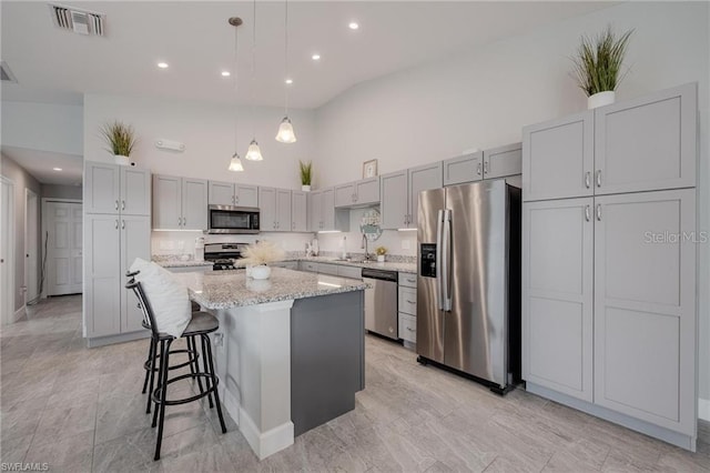 kitchen with light stone counters, visible vents, a towering ceiling, appliances with stainless steel finishes, and a kitchen island