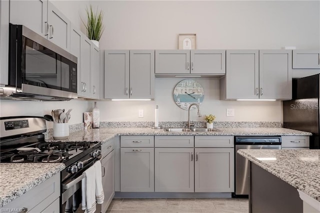 kitchen with light stone countertops, appliances with stainless steel finishes, gray cabinets, and a sink