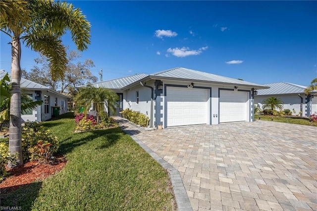 single story home with decorative driveway, stucco siding, a front yard, metal roof, and a garage