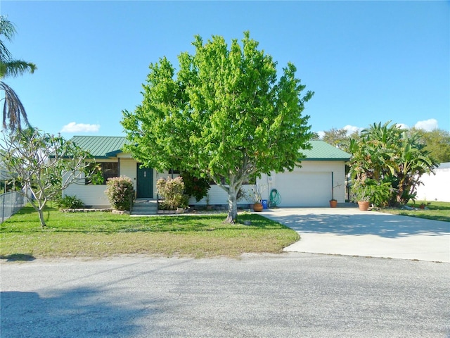 view of property hidden behind natural elements with metal roof, a front lawn, an attached garage, and driveway