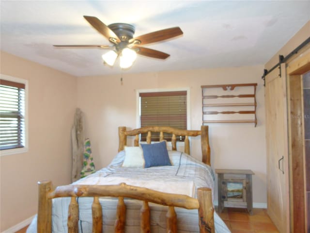 bedroom featuring a ceiling fan, light tile patterned flooring, baseboards, and a barn door