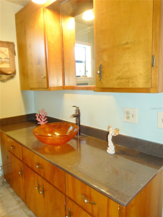 kitchen with light tile patterned floors, brown cabinetry, dark stone countertops, and a sink