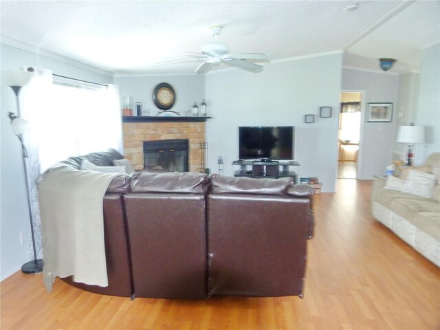 living room with a ceiling fan, crown molding, a stone fireplace, and light wood finished floors