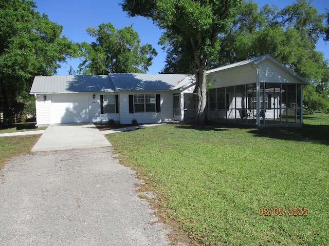 ranch-style house featuring a front lawn, concrete driveway, metal roof, a sunroom, and an attached garage