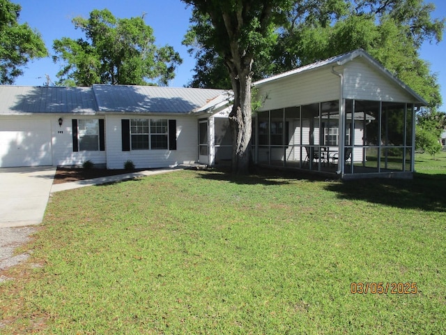 ranch-style home with a front yard, driveway, an attached garage, a sunroom, and metal roof