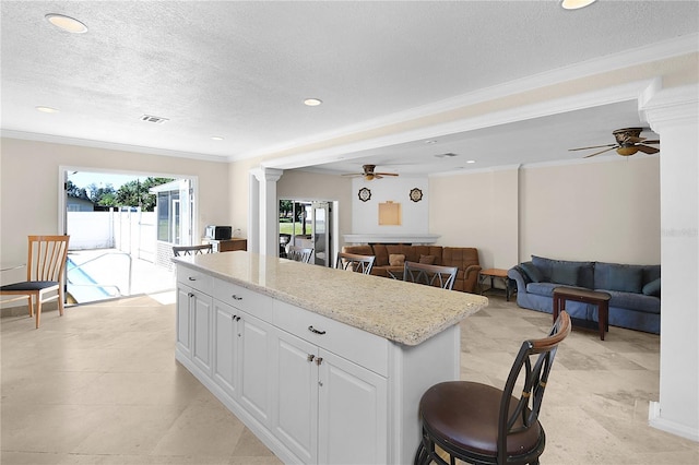 kitchen with visible vents, a kitchen island, ornamental molding, ceiling fan, and white cabinets