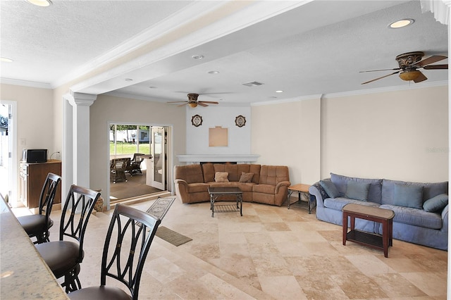 living room with a ceiling fan, visible vents, decorative columns, ornamental molding, and a textured ceiling