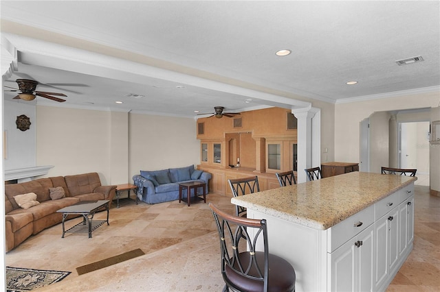 kitchen with a ceiling fan, visible vents, white cabinets, crown molding, and open floor plan