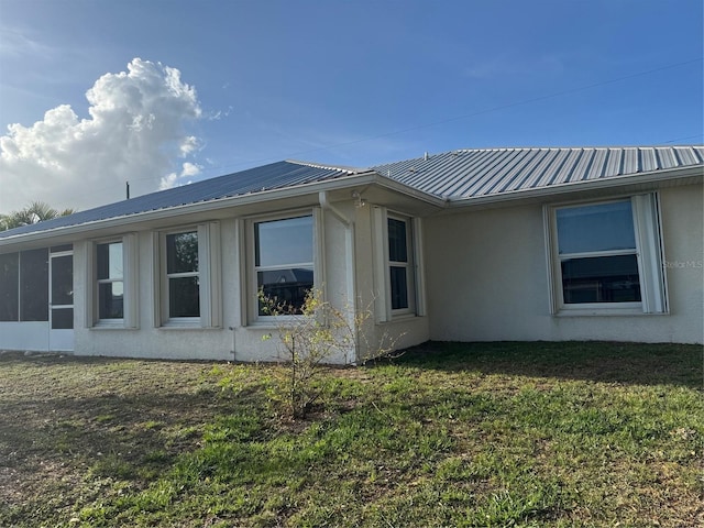 view of side of home with a lawn, metal roof, a sunroom, and stucco siding