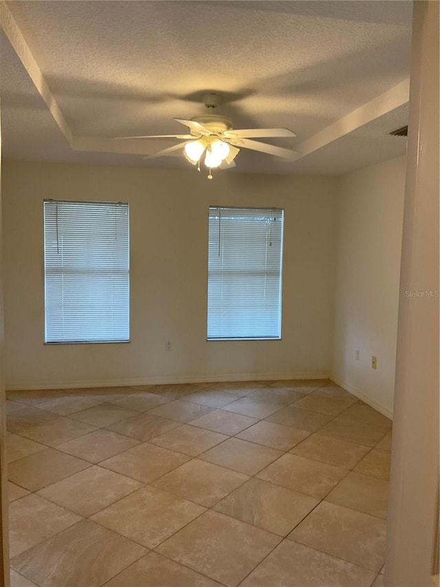 unfurnished room with baseboards, ceiling fan, a textured ceiling, a tray ceiling, and light tile patterned floors