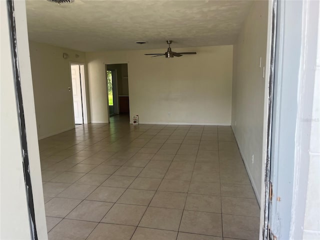 empty room with ceiling fan, light tile patterned floors, a textured ceiling, and baseboards