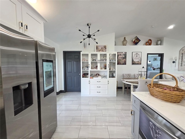 7935 NW 90th Ct, Okeechobee, FL 34972 - kitchen with stainless steel appliances, lofted ceiling, light stone counters, white cabinets, and a chandelier