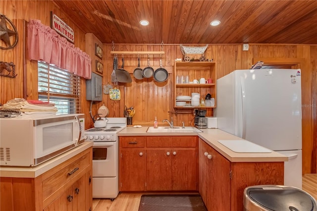 kitchen with wooden walls, white appliances, kitchen peninsula, and sink