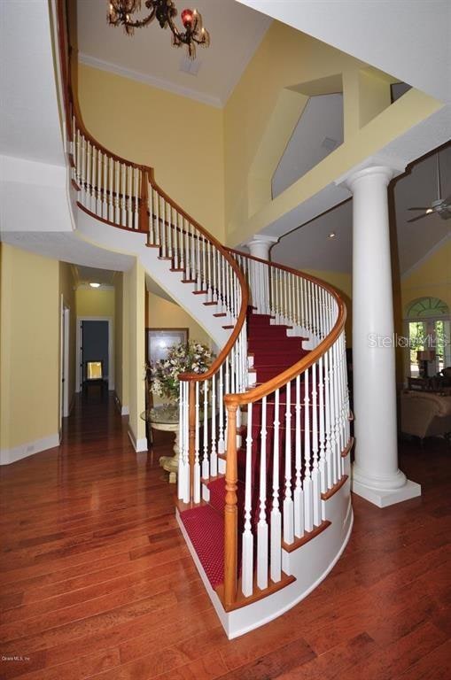 stairway featuring a towering ceiling, decorative columns, ceiling fan, and dark hardwood / wood-style floors