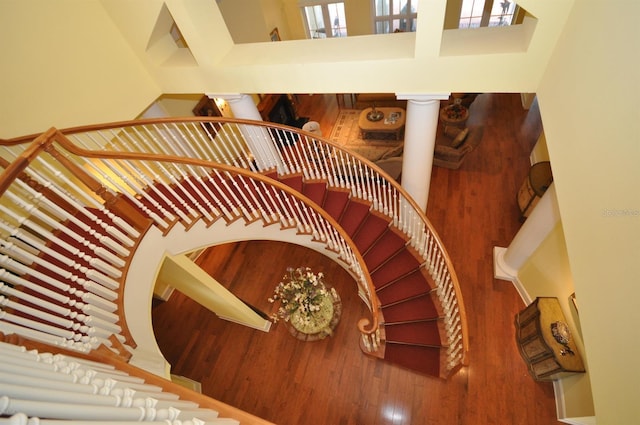 stairway with a high ceiling, wood-type flooring, and decorative columns