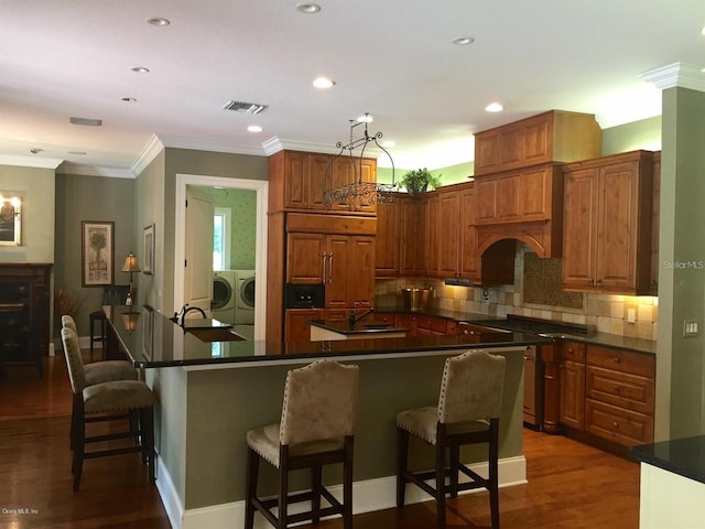 kitchen featuring ornamental molding, a breakfast bar area, washer and clothes dryer, backsplash, and dark hardwood / wood-style flooring