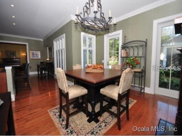 dining area with an inviting chandelier, plenty of natural light, crown molding, and dark wood-type flooring