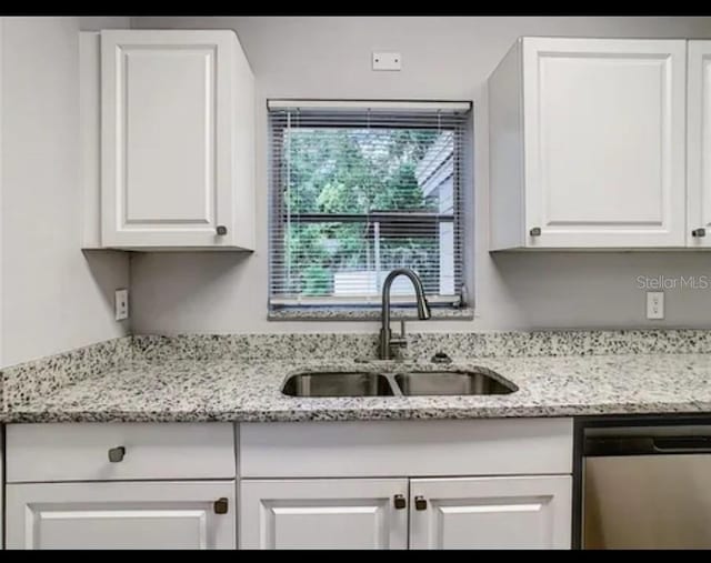 kitchen featuring white cabinets, stainless steel dishwasher, light stone countertops, and sink