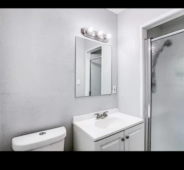 bathroom with toilet, an enclosed shower, and vanity