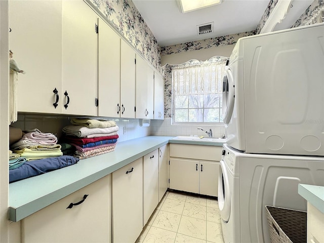 laundry area featuring stacked washer and dryer, cabinets, sink, and light tile floors