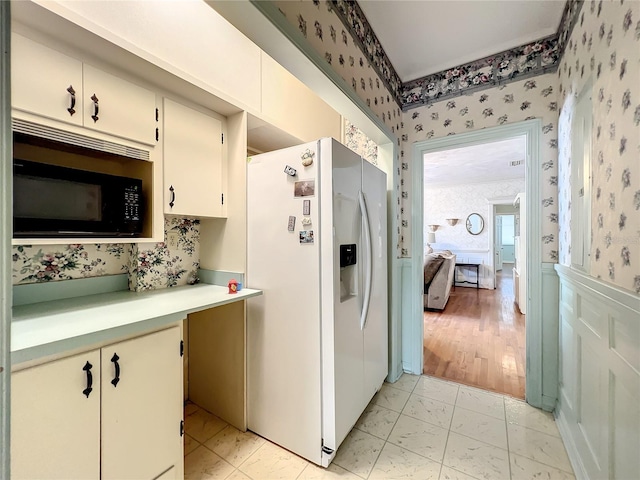 kitchen with white refrigerator with ice dispenser, light wood-type flooring, white cabinets, and black microwave