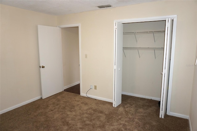 unfurnished bedroom featuring a closet, a textured ceiling, and dark colored carpet