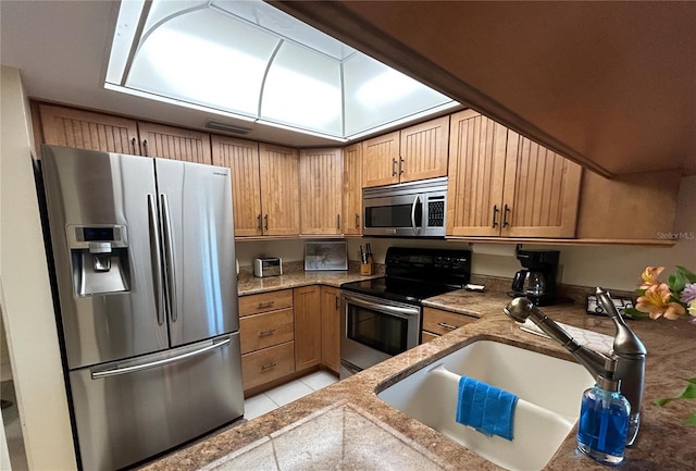 kitchen featuring light tile patterned flooring, sink, appliances with stainless steel finishes, and a skylight