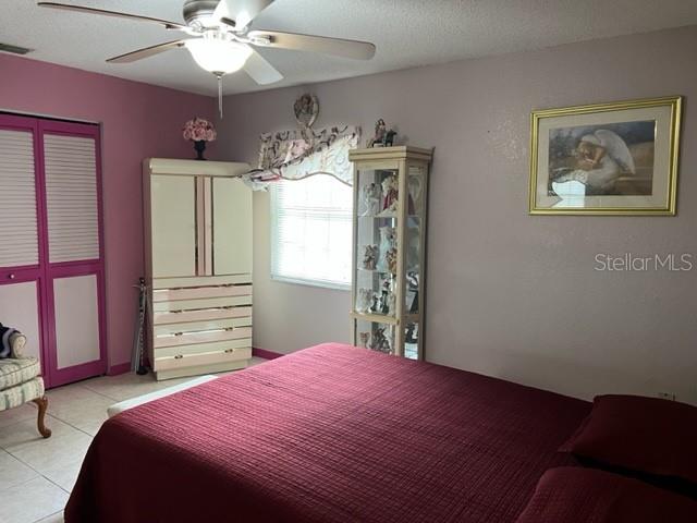 bedroom with a textured ceiling, light tile flooring, and ceiling fan