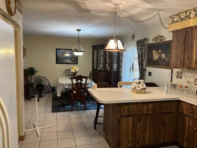 kitchen with decorative light fixtures, light tile floors, a breakfast bar area, and dark brown cabinets