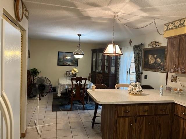 kitchen with a kitchen bar, decorative light fixtures, dark brown cabinetry, and light tile flooring