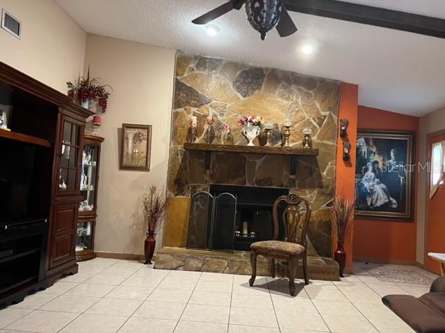 living area with light tile floors, vaulted ceiling, ceiling fan, a textured ceiling, and a stone fireplace