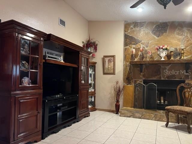 living area with light tile floors, a stone fireplace, ceiling fan, and a textured ceiling