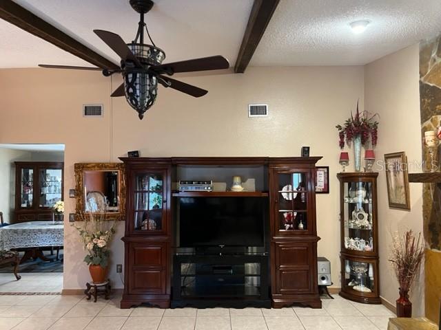 tiled living room with a textured ceiling, ceiling fan, and beamed ceiling