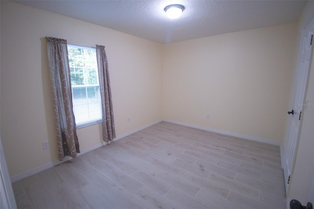 empty room with a textured ceiling and light hardwood / wood-style flooring