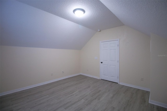 additional living space with a textured ceiling, light hardwood / wood-style floors, and vaulted ceiling