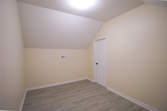 additional living space featuring lofted ceiling, a textured ceiling, and light hardwood / wood-style floors