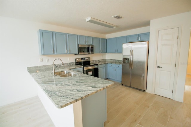 kitchen featuring kitchen peninsula, blue cabinets, sink, light stone counters, and stainless steel appliances